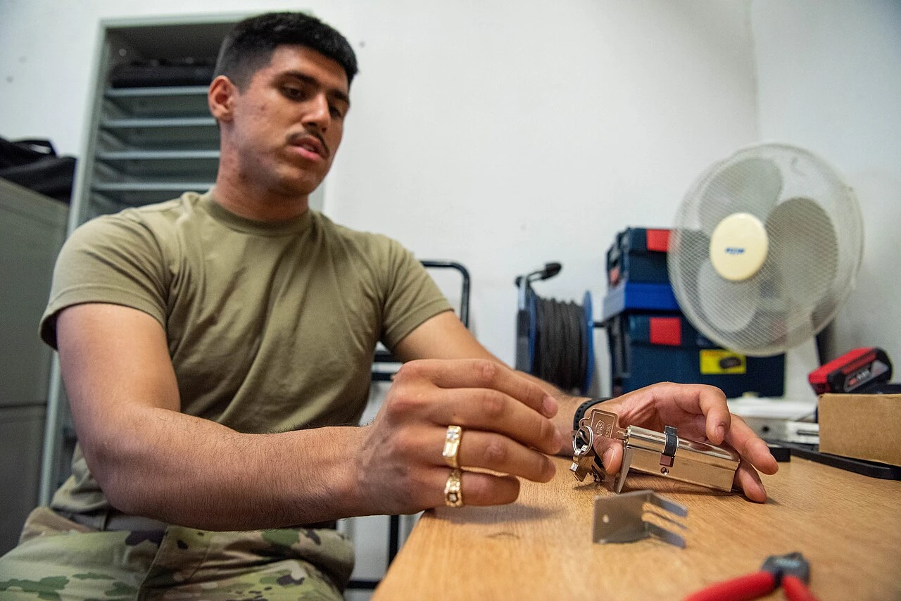 Locksmith at a workbench fitting a key into a lock cylinder he has just rekeyed