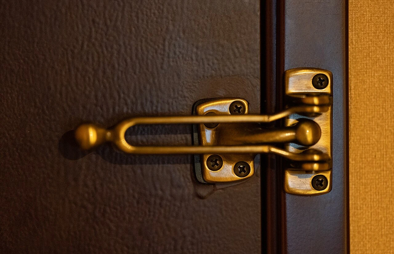 Brass swing bar security latch on the inside of a dark wood rental unit door